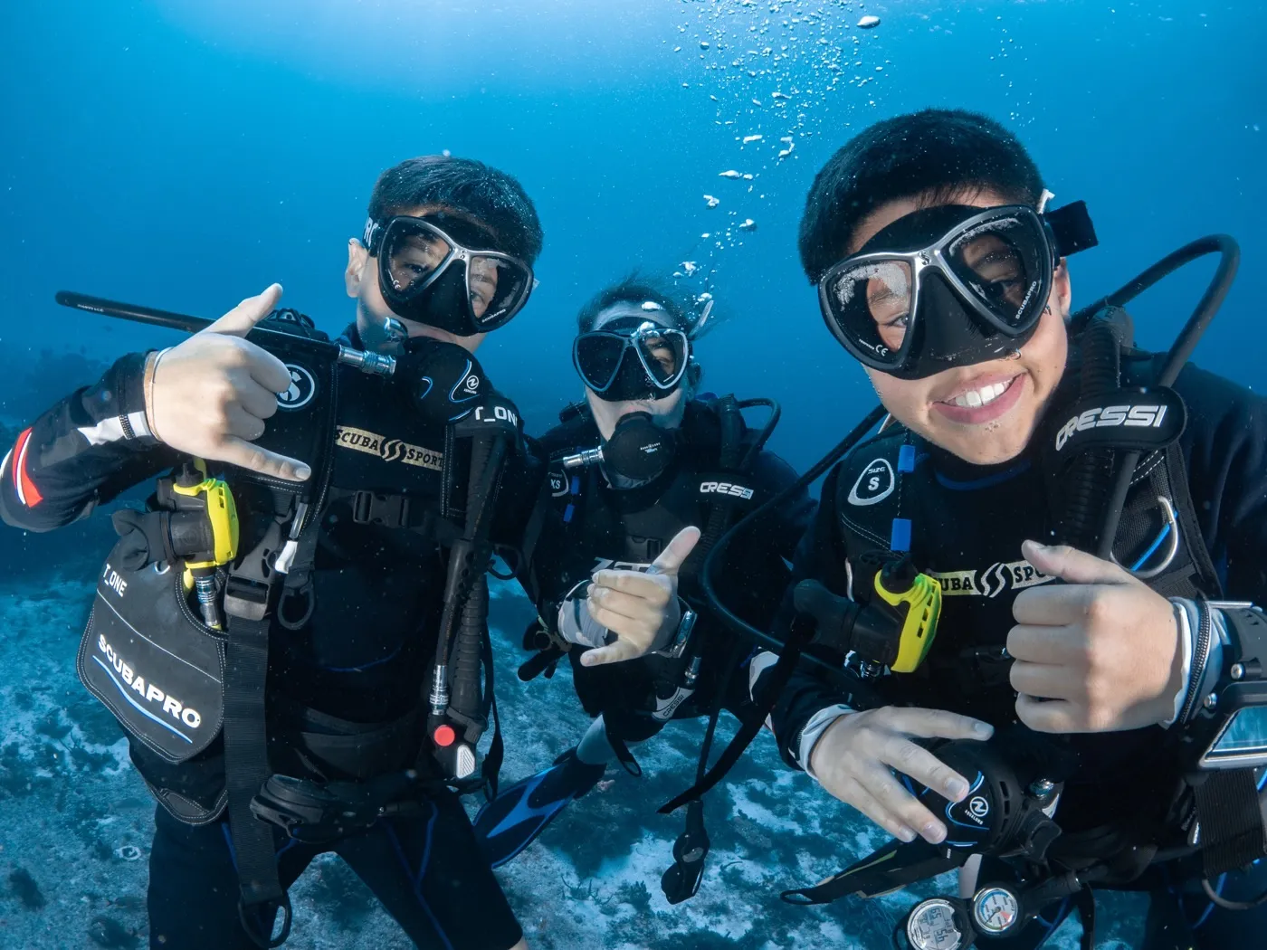 Tres buzos del grupo bajo el agua, con el pulgar arriba