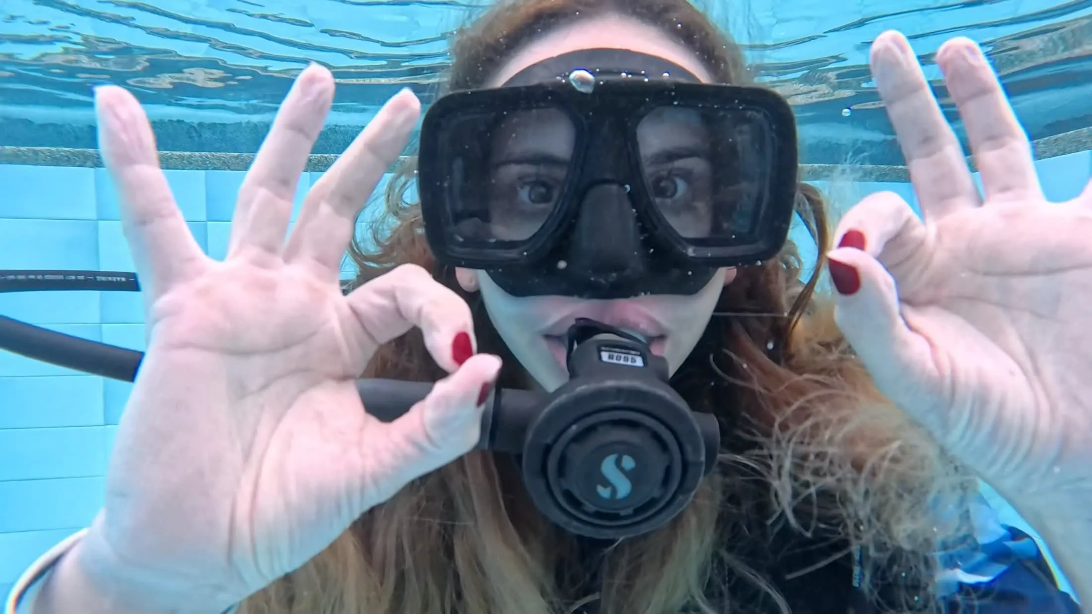 Una alumna hace la señal de OK bajo el agua en la piscina, durante su bautismo de buceo en Bogotá