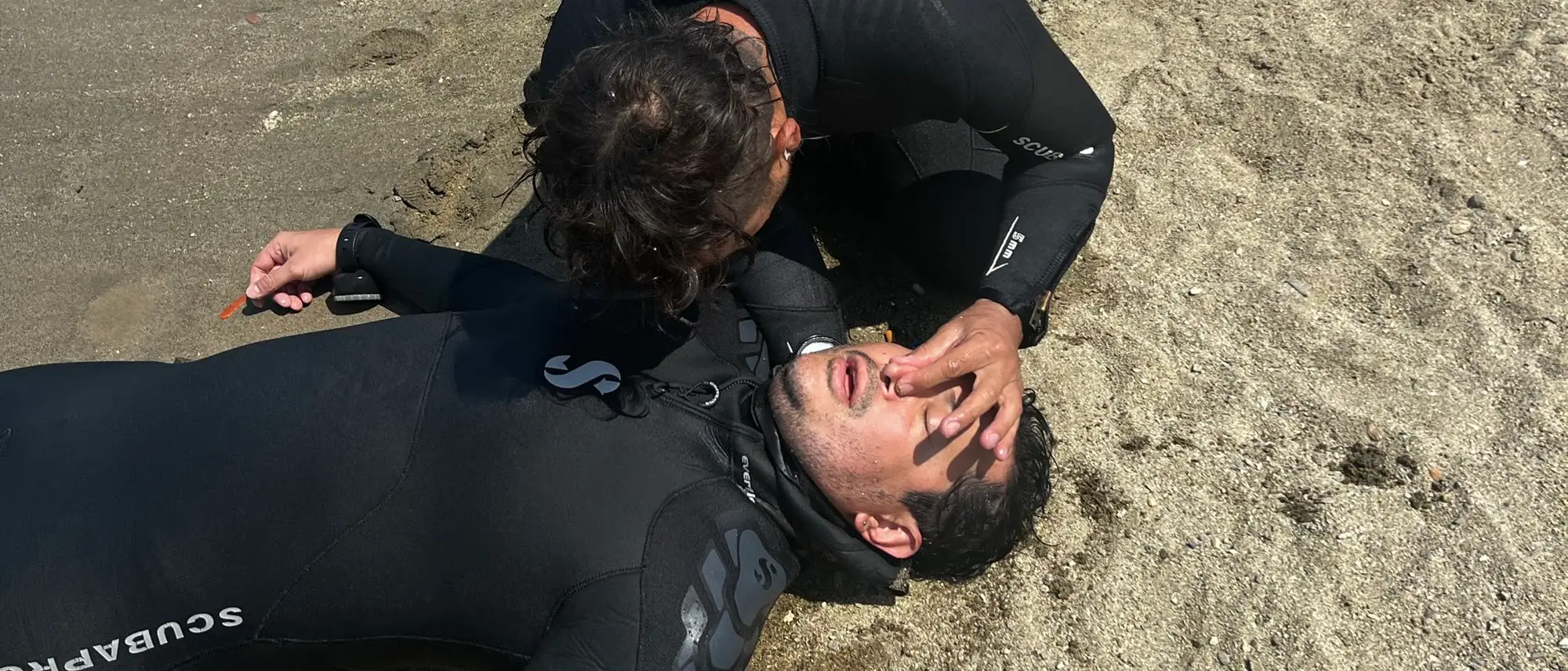 Un simulacro de rescate en la orilla: un buzo evalúa a su compañero tendido en la arena